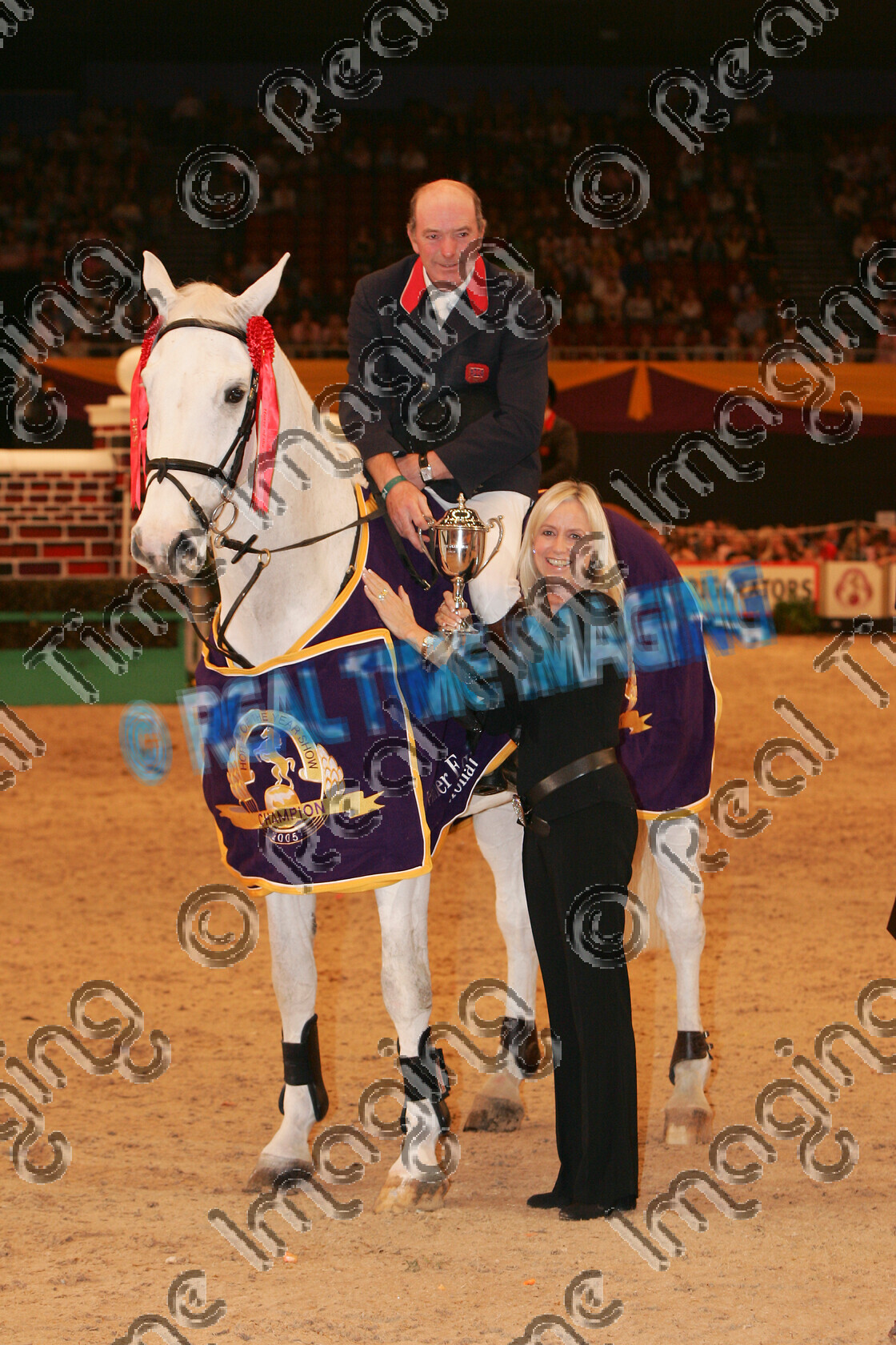 S05-67-12-069 
 HOYS 2005: The Horse Of The Year Show Puissance Winner 
 Keywords: horse of the year show 2005 05 hoys saturday 15 10 october showjumping showjumper 23 Puissance Winner 2 Lactic John Whitaker grey gray gelding standing presentation rug trophy rosette